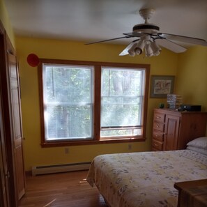A bedroom with two windows, a ceiling fan, a bed with a floral bedspread, and a dresser. - Spacious Lakefront home on Moose Pond (Bridgton)