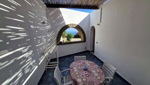 Une petite terrasse extérieure avec une table et des chaises, une vue à travers une arche et une nappe à motifs.