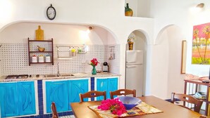 Une cuisine avec des meubles de rangement bleus, une table à manger avec des chaises et un tableau accroché au mur.