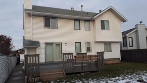 A two-story house with a front deck, a wooden bench, and a metal gate. - Entire 4 Bedroom Home with easy access (Edmonton)