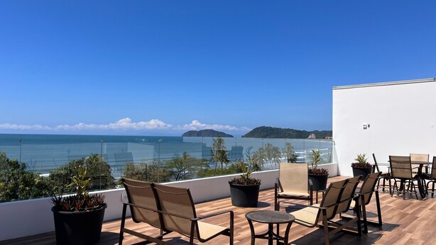 A balcony with outdoor seating, potted plants, and a view of the sea and distant islands. - Ocean view Condo - Best beach location (Jaco)