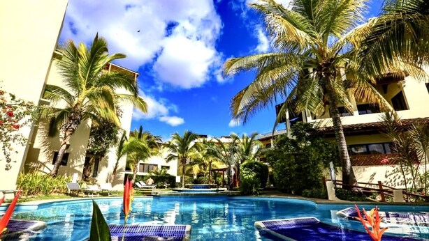 Una piscina con piastrelle blu, circondata da palme e lettini.