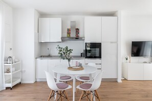 Une cuisine moderne avec des meubles blancs, une table à manger avec quatre chaises et un téléviseur posé sur un meuble blanc.