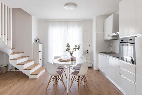 Une cuisine moderne avec des meubles blancs, un four en acier inoxydable et un coin repas comprenant une table ronde et des chaises.