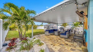 An outdoor patio area with a covered seating arrangement, a grill, and a pool.