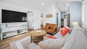 A modern living room with a flat-screen TV, leather chairs, a sofa, and a kitchen area in the background.