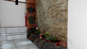 A corner with tiled flooring, a brick wall, and a shelf with potted plants and flowers.