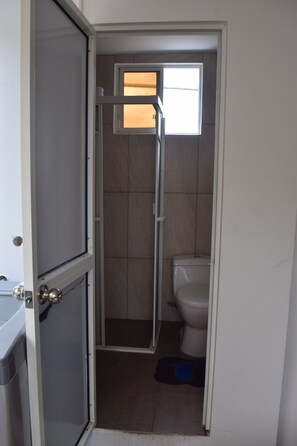 A bathroom with a shower, toilet, and a window providing natural light.