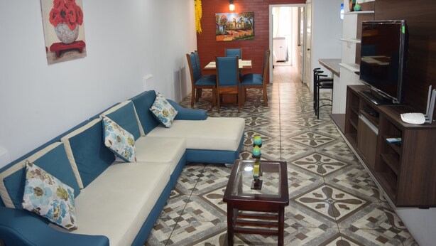 A living room with a sofa, coffee table, TV, and a dining area with chairs and a table.