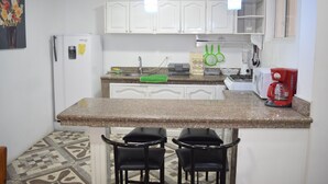 A kitchen with white cabinets, a granite countertop, a refrigerator, a coffee maker, and two black chairs.