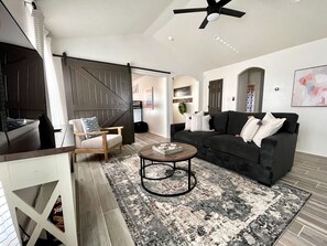 A living room with a dark-colored sofa, a wooden chair, a coffee table, and a patterned rug. - Home 7 min to Lackland AFB & close to SeaWorld (San Antonio)