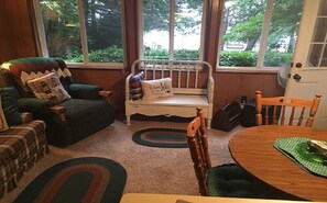 Relax in this inviting living room with a comfortable armchair, bench, and dining table, surrounded by lush greenery.