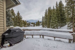 Un barbecue couvert et une bouteille de propane se trouvent à l’extérieur d’une maison, sur un terrain et des arbres recouverts de neige.