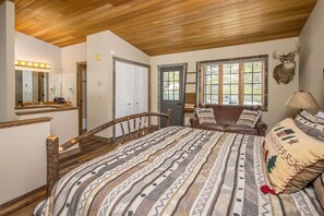 Une chambre avec un lit en bois, un grand miroir, une décoration représentant une tête de cerf et une fenêtre donnant sur la forêt.