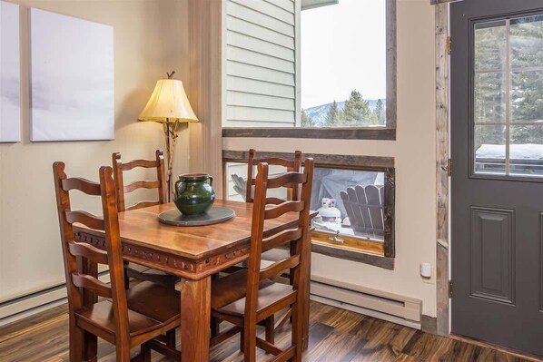 Un coin repas avec une table et des chaises en bois, une lampe et une fenêtre donnant sur une terrasse et des arbres.