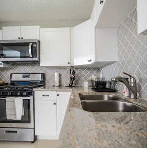 A modern kitchen with white cabinets, a stainless steel microwave, a gas stove, and a double sink.