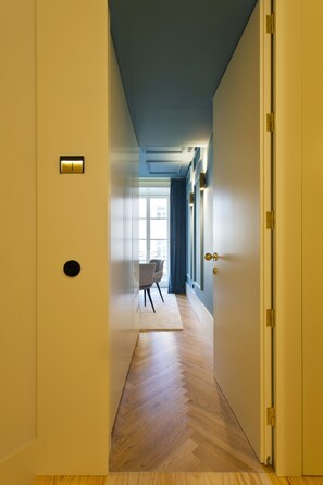 A hallway with a wooden floor, a door on the right, and a chair in the distance.