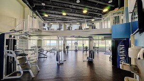 Une salle de sport équipée de divers appareils d’exercice, dotée d’une mezzanine et de grandes fenêtres.