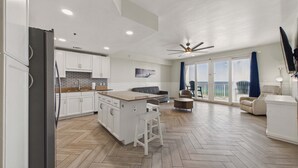 Une cuisine moderne avec des meubles blancs, un parquet en bois disposé en chevrons et un grand îlot central doté de tabourets.