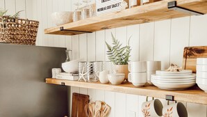 Una cocina con armarios blancos, estantes de madera y distintos utensilios de cocina.