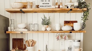 Una cocina con armarios blancos, estantes de madera y un cartel que promociona una cuenta de Instagram.