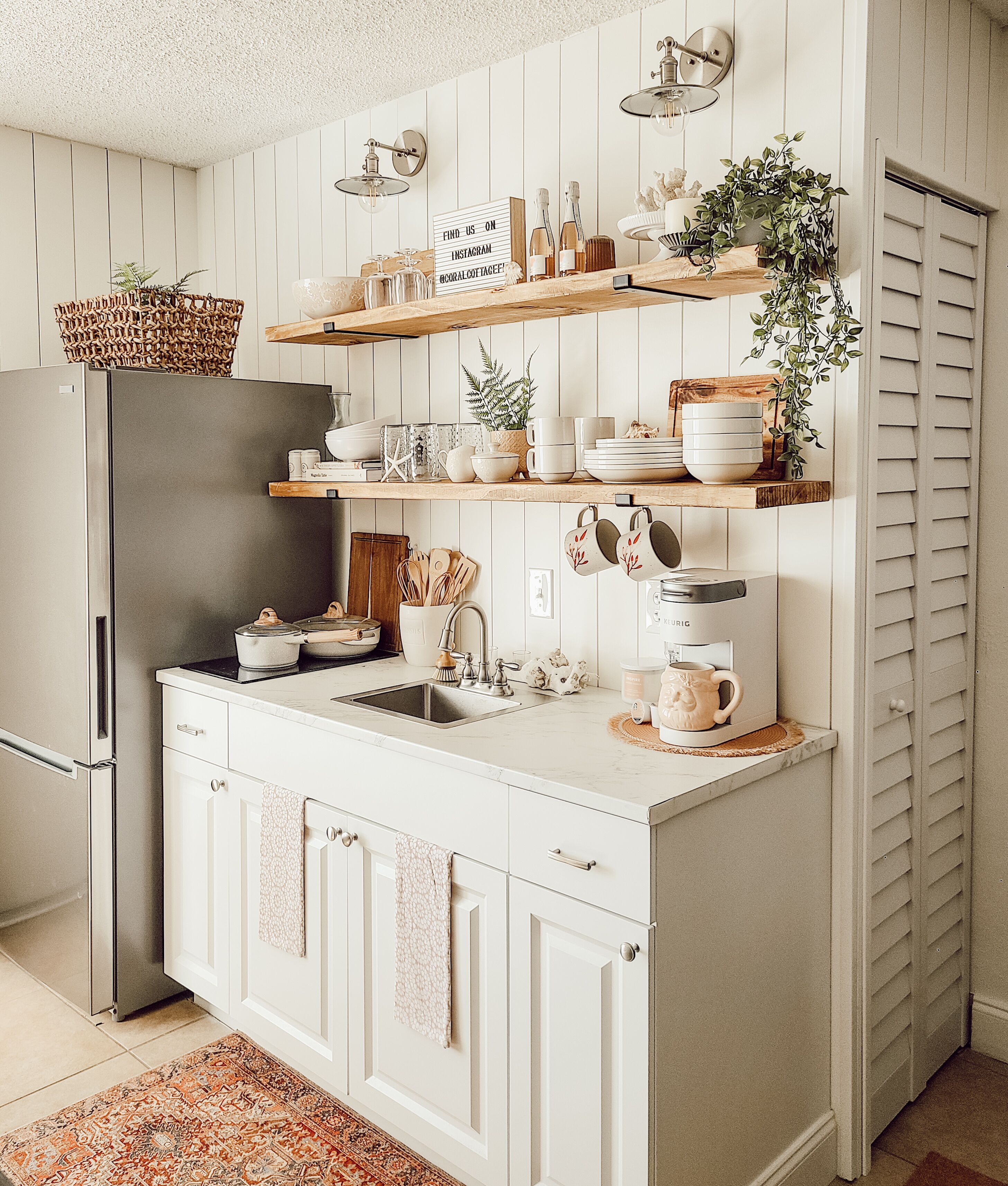 A kitchen with white cabinetry, a built-in refrigerator, a coffee maker, and various kitchen utensils on open shelves.