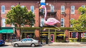 A street view with a pink flamingo sculpture on a pole, a brick building with storefronts, and a parked car. - Artistic Abode Close to MICA & Johns Hopkins (Baltimore)