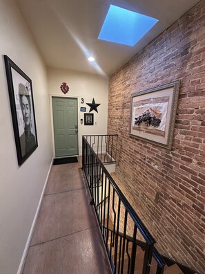 Un pasillo con tragaluz, una puerta verde, un adorno con forma de estrella y un cuadro en la pared.
