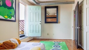 A bedroom with a bed, a green rug, a door, and a window. - Artistic Abode Close to MICA & Johns Hopkins (Baltimore)