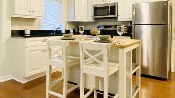 Una cocina moderna con armarios blancos, un refrigerador de acero inoxidable y una mesa de comedor de madera con dos sillas.
