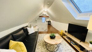 Un loft moderno con un sofá de cuero negro, una mesa de centro redonda de madera y un televisor sobre un soporte de madera.