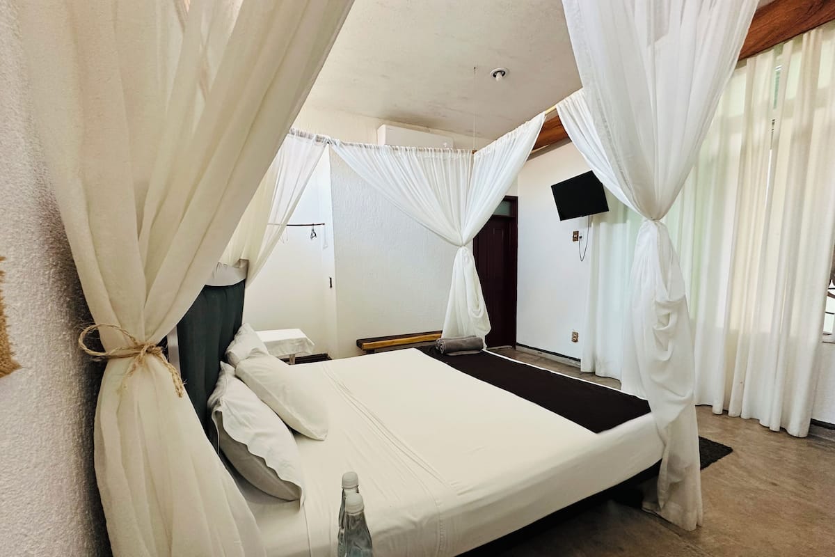 A bed with white linens, a water bottle on the side, and white curtains.
