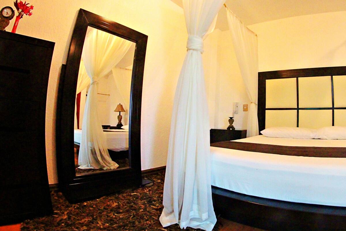 A bedroom with a large bed, a nightstand, a mirror, and a dark wooden headboard.