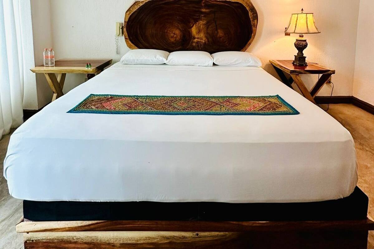 A hotel room with a large bed, a wooden headboard, a bedside table with a lamp, and a small table with bottles.