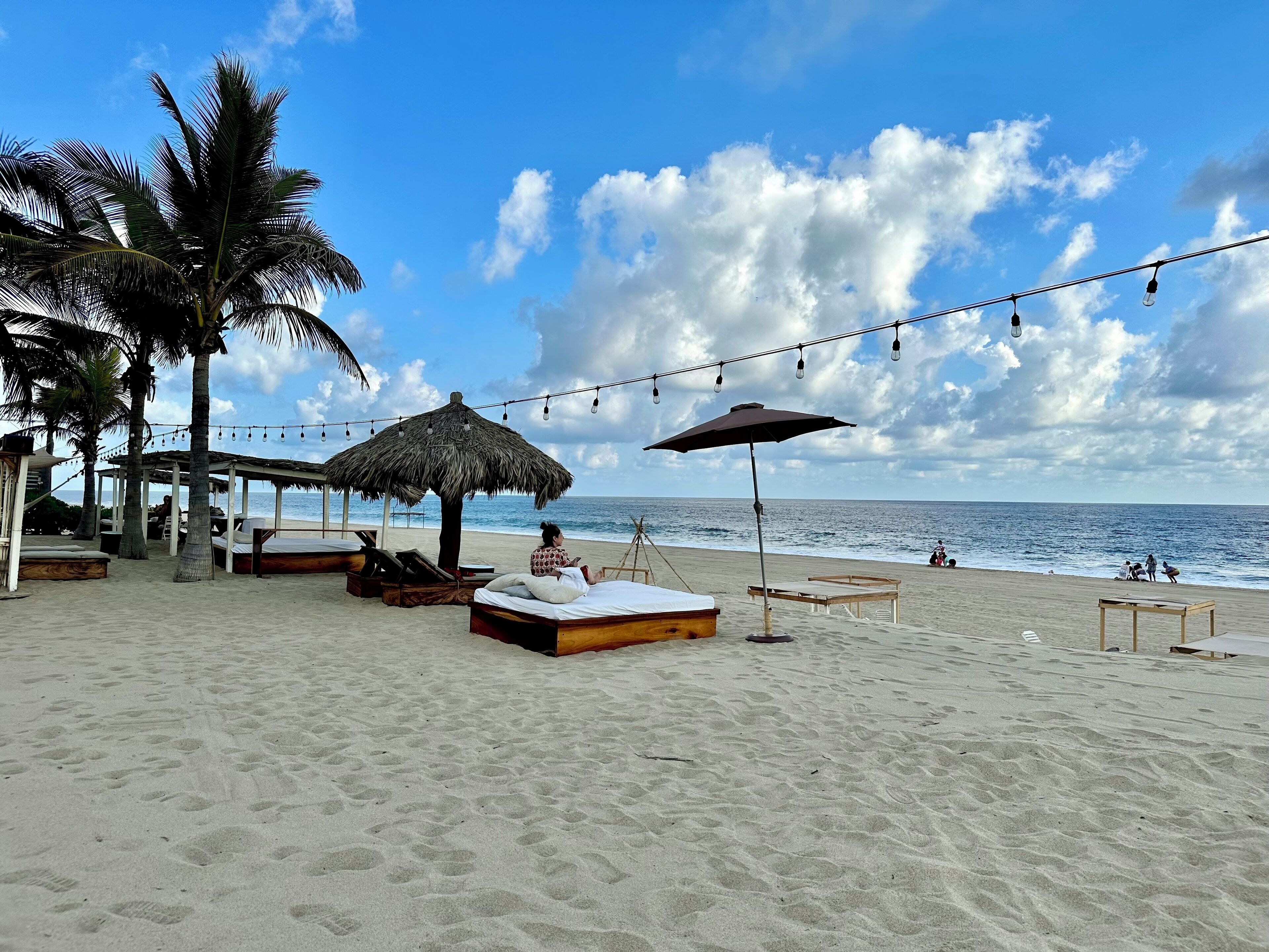 Une plage avec des parasols en chaume, des chaises longues en bois et une vue sur l’océan.