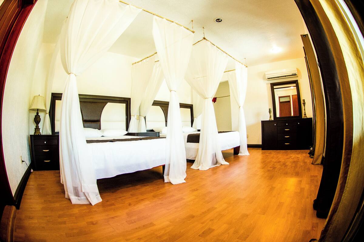 A bedroom with a four-poster bed, a nightstand, a dresser, and a mirror.