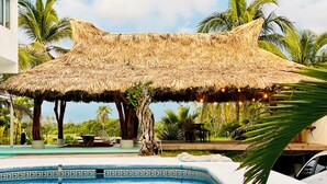 A pool area with a thatched roof structure, palm trees, and a tiled pool. - Hotel Boutique Punta Jamaica (Coyuca de Benitez)