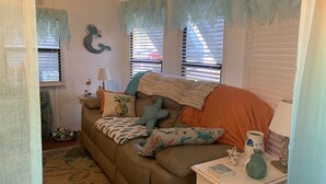 Una sala de estar acogedora con un sofá marrón, cojines decorativos, un tapete estampado y una mesita de noche con una lámpara y un jarrón.