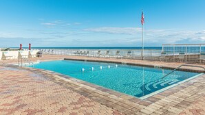A swimming pool with a flag, lounge chairs, and a view of the ocean. - WEEKLY SUMMER SPECIALS! Oceanfront Condo - Heated Pool - NO DRIVE BEACH (Daytona Beach Shores)