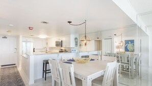 A modern kitchen with white cabinetry, a central island, and a dining area with a white table and chairs. - WEEKLY SUMMER SPECIALS! Oceanfront Condo - Heated Pool - NO DRIVE BEACH (Daytona Beach Shores)