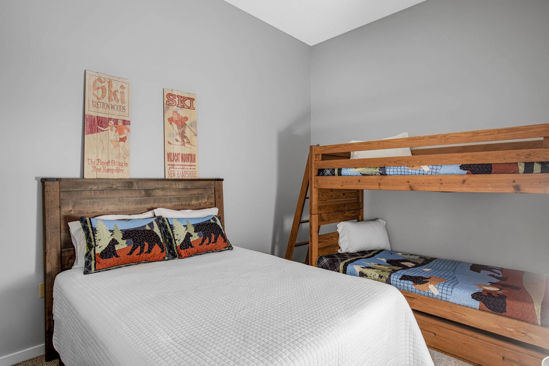 A bedroom with a wooden bunk bed, a single bed with patterned pillows, and two vintage ski-themed posters on the wall.