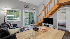A modern living room with a wooden staircase, a dining area with a table set for a meal, and a cozy seating area with a sofa. - Loon Escape (Lincoln)