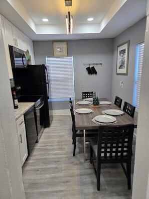A modern kitchen with a dining area, featuring a black refrigerator, stainless steel appliances, and a wooden dining table set for four.