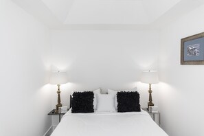 A neatly made bed with white bedding, flanked by two bedside tables with lamps and decorative items.
