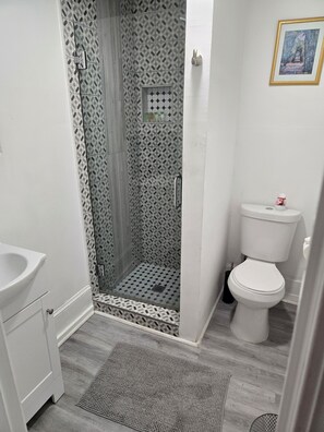A bathroom with a shower, toilet, sink, and a patterned wall.
