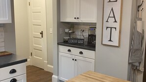 Una cocina con armarios blancos, un letrero que indica barra de café y una mesa de madera.