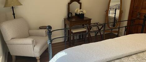 A bedroom with a bed, a chair, a desk with a mirror, and a lamp.