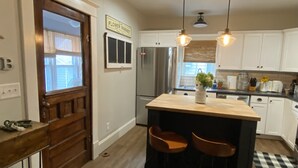 Una cocina con armarios blancos, una isla de madera con taburetes, un refrigerador de acero inoxidable y un letrero de mercado de flores.
