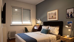Een slaapkamer met een bed, een bureau, een stoel, een radiator en een raam met zonwering.