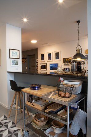 A modern kitchen with a wooden table, metal shelves, and a hanging light fixture.